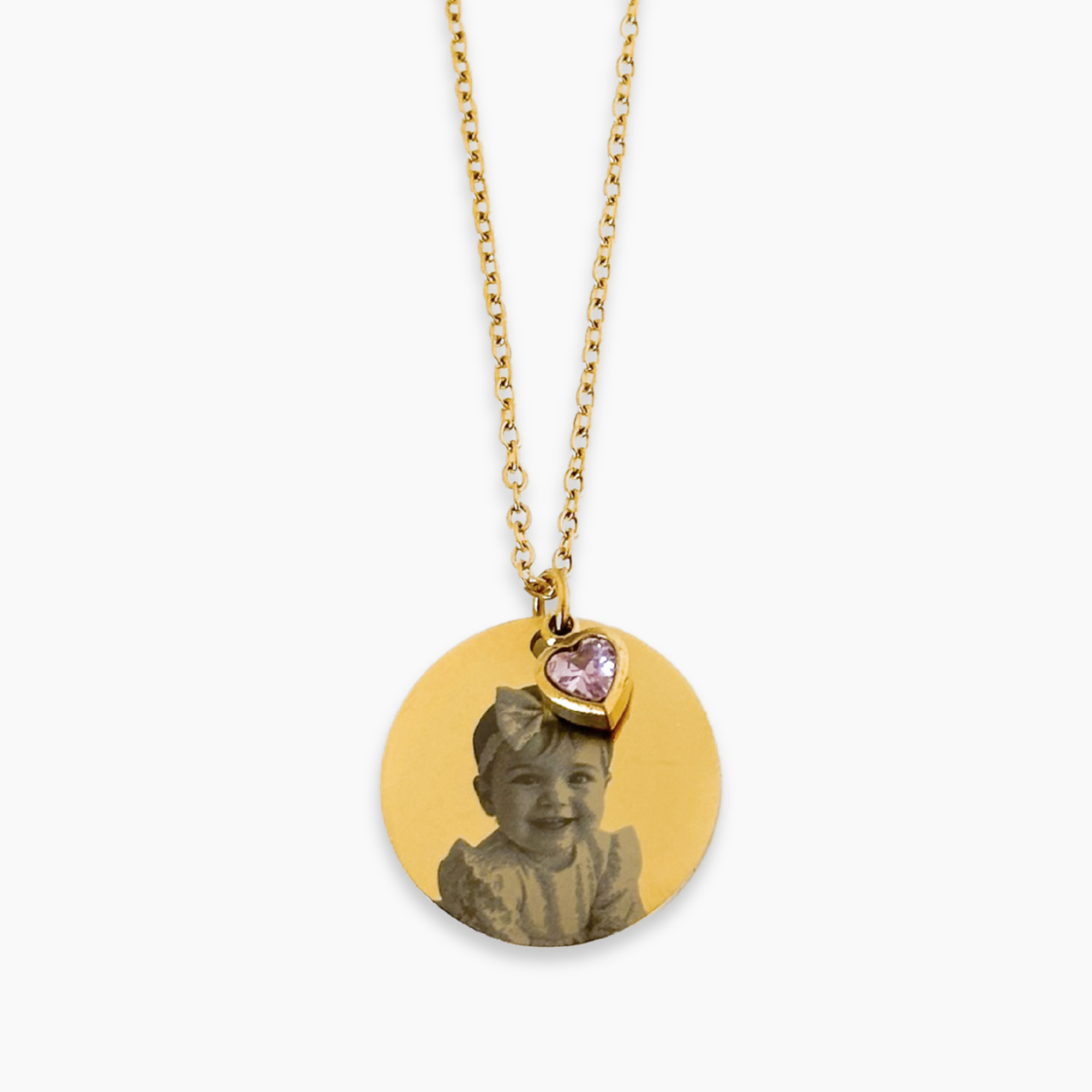 A personalized necklace with a gold-plated round disk, a chain, and an engraved photo of a baby wearing a pink bow.